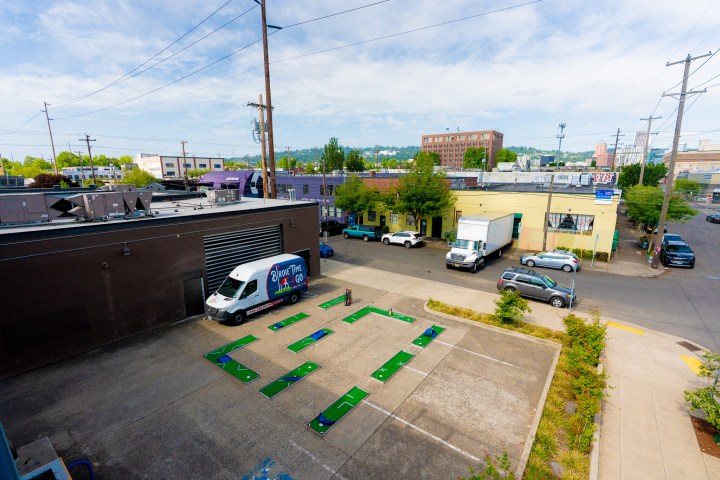 Aerial view of a 9-hole mini golf course set up in a parking lot with colorful obstacles and pathways.