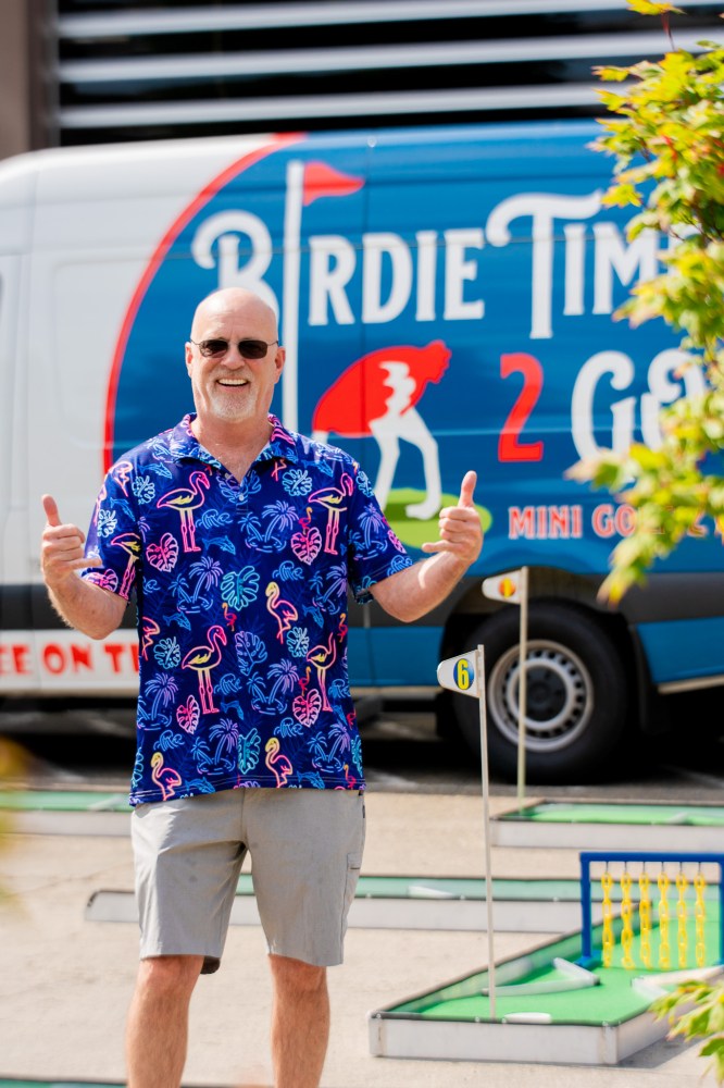 a man standing in front of van for traveling mini golf course