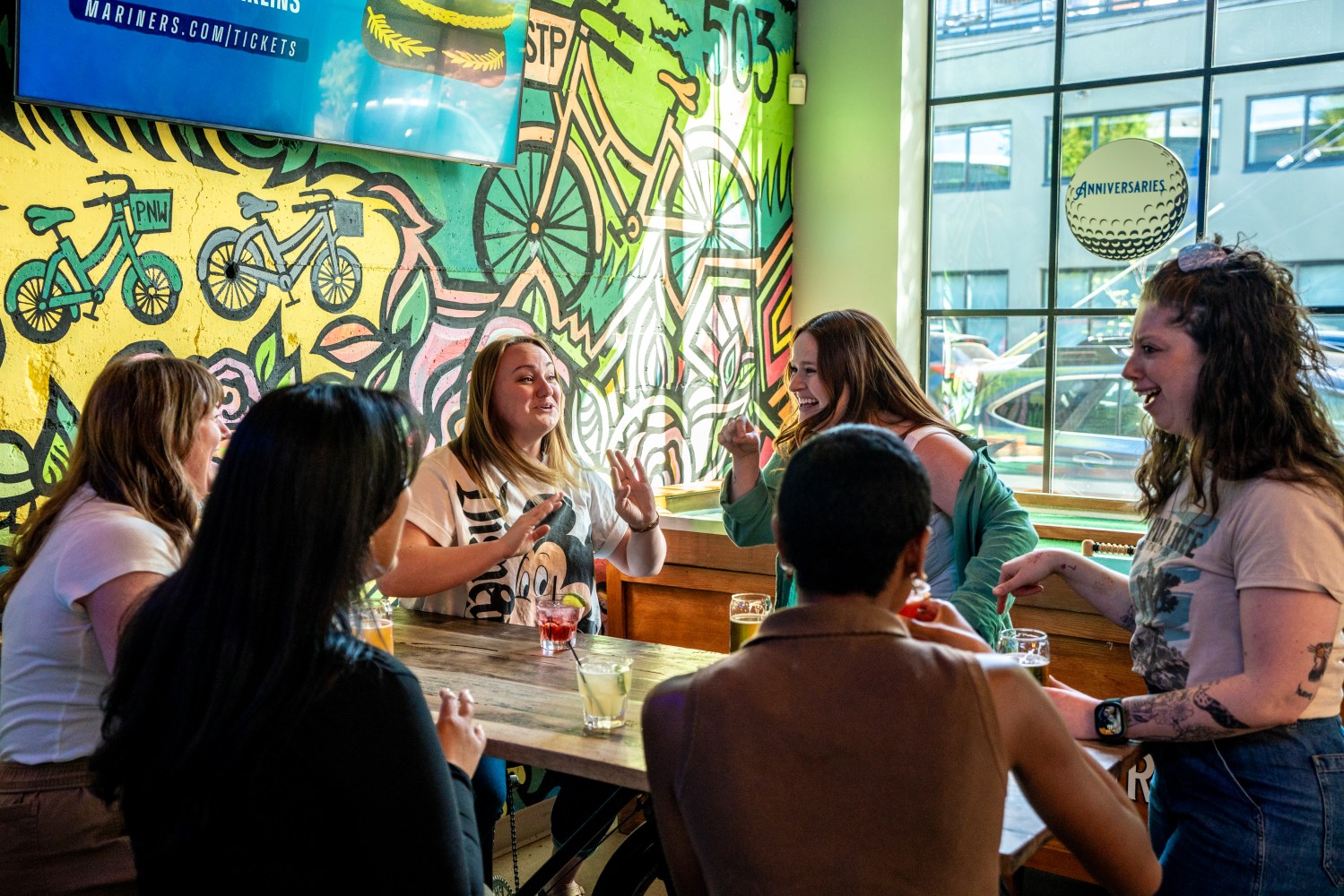 Group of coworkers having fun at a mini golf  bar with colorful mural background.