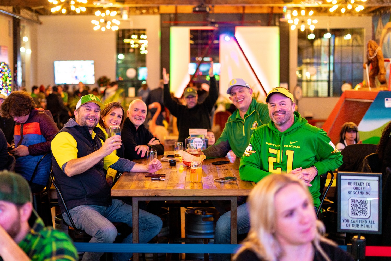 Group of Oregon Duck Fans smiling and sitting at a table in a lively restaurant.