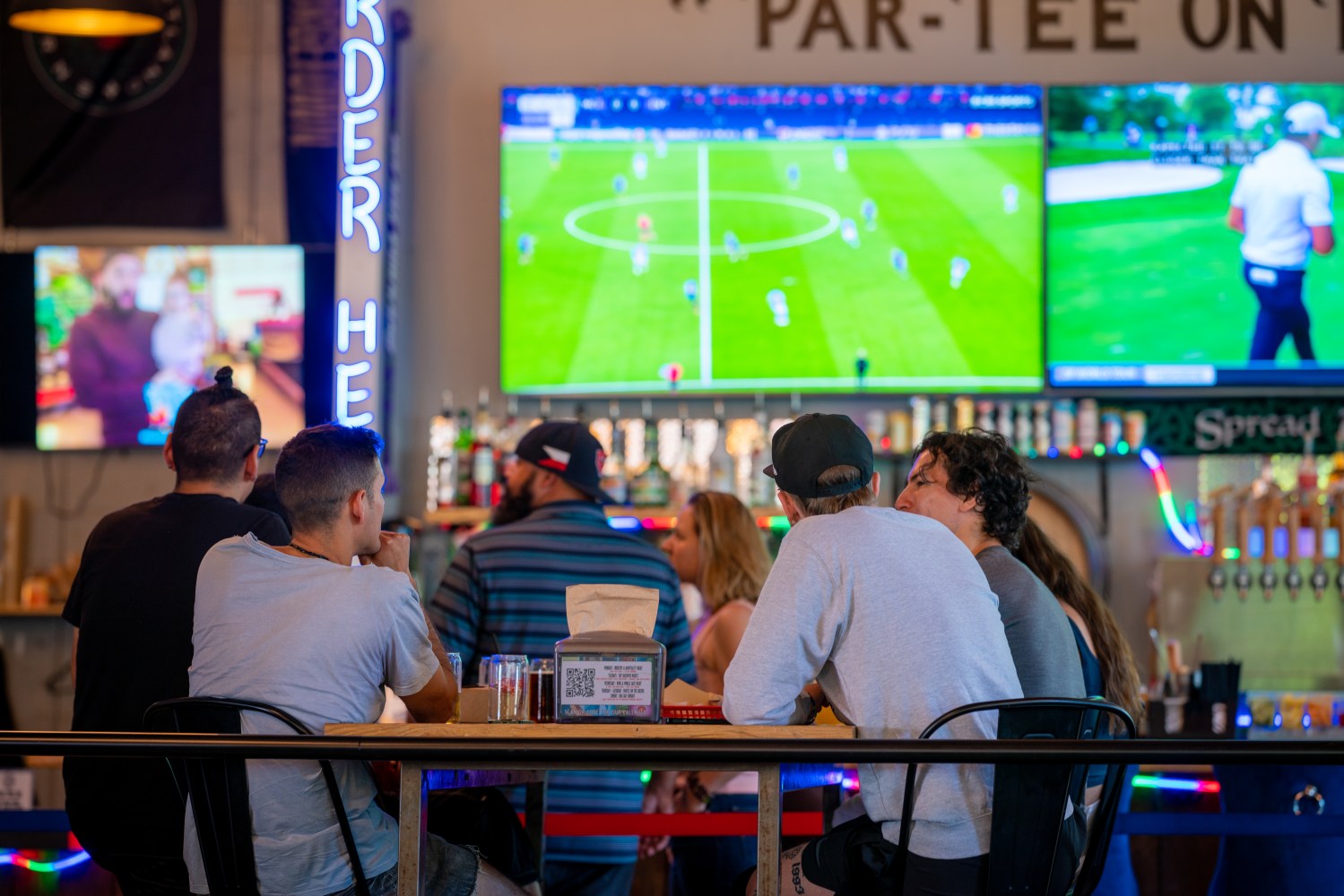 People sitting at a bar watching multiple TV screens showing sports.
