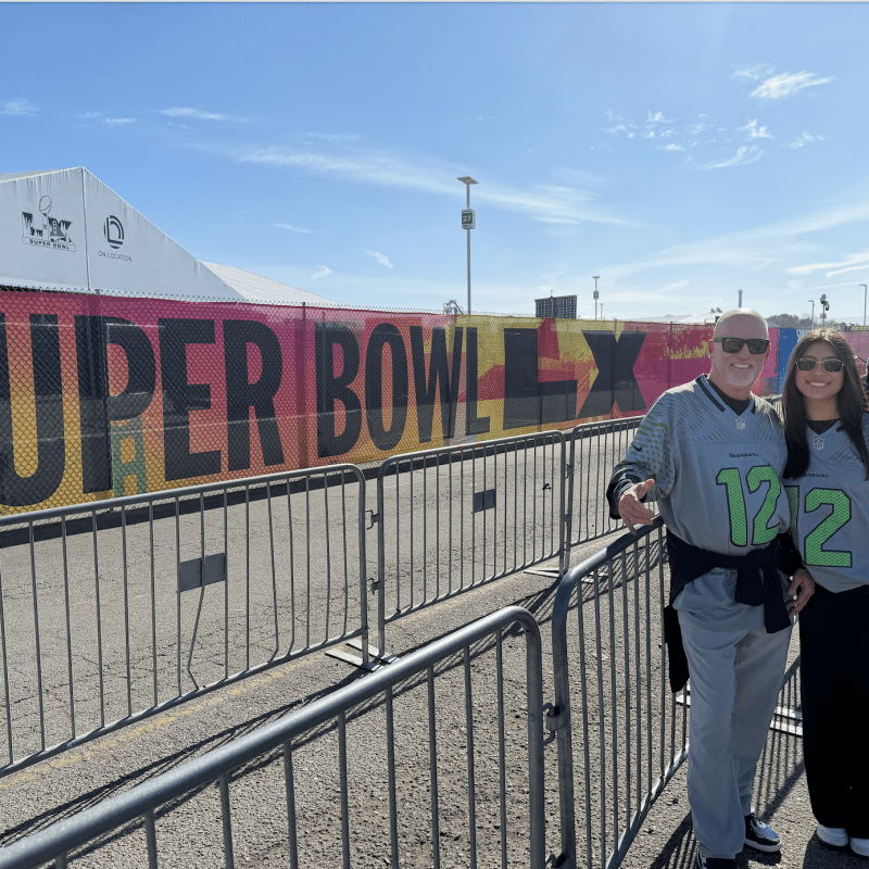Two people in matching shirts stand by a Super Bowl LVII sign.