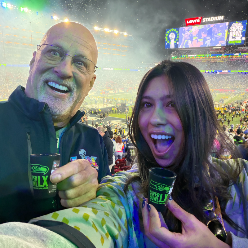 Two people smiling at a football stadium during an event.