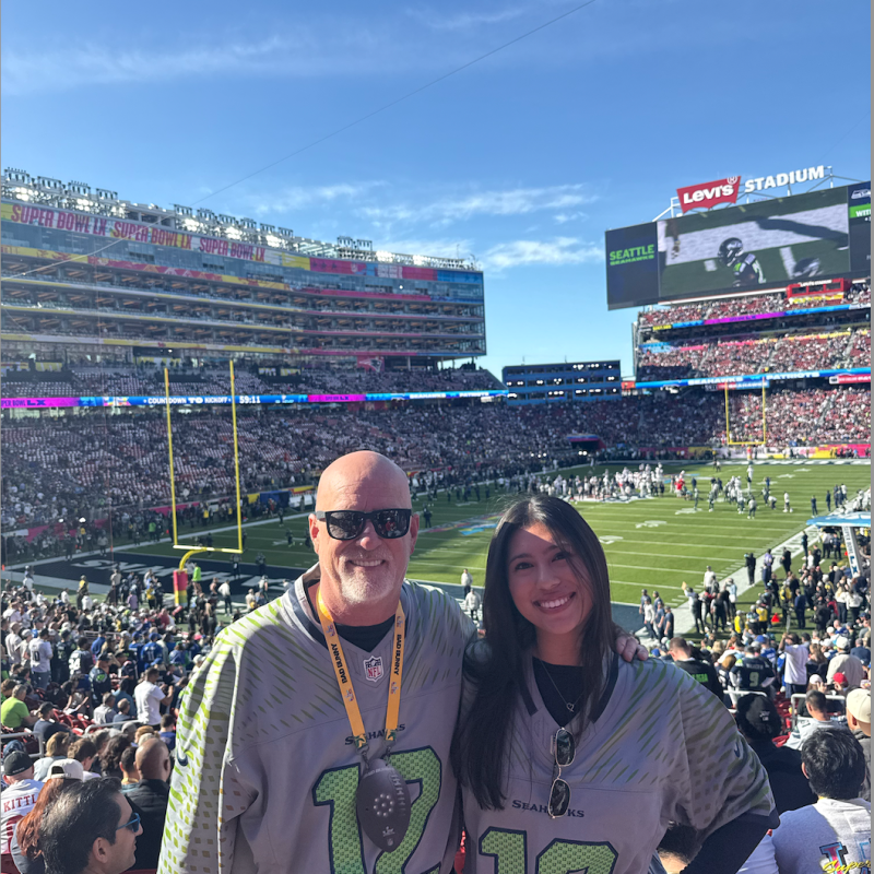 Two people in sports jerseys smiling at a football stadium.