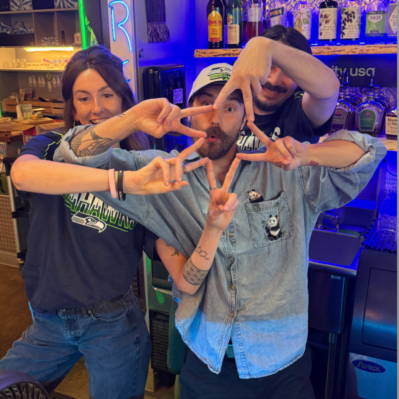 Three people behind a bar making peace signs with hands intersecting.